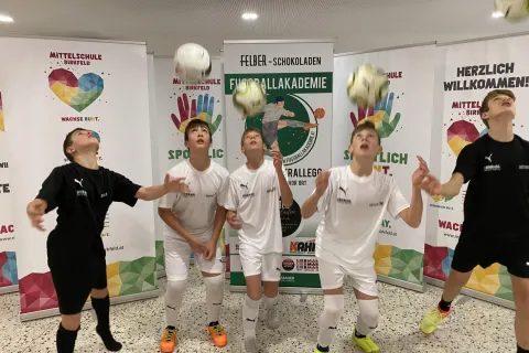 Schüler der Fußballakademie köpfeln Bälle vor den Fahnen der Mittelschule Birkfeld