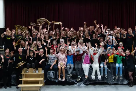 Große Gruppe von Schülerinnen und Schülern mit Instrumenten auf einer Bühne, alle jubeln