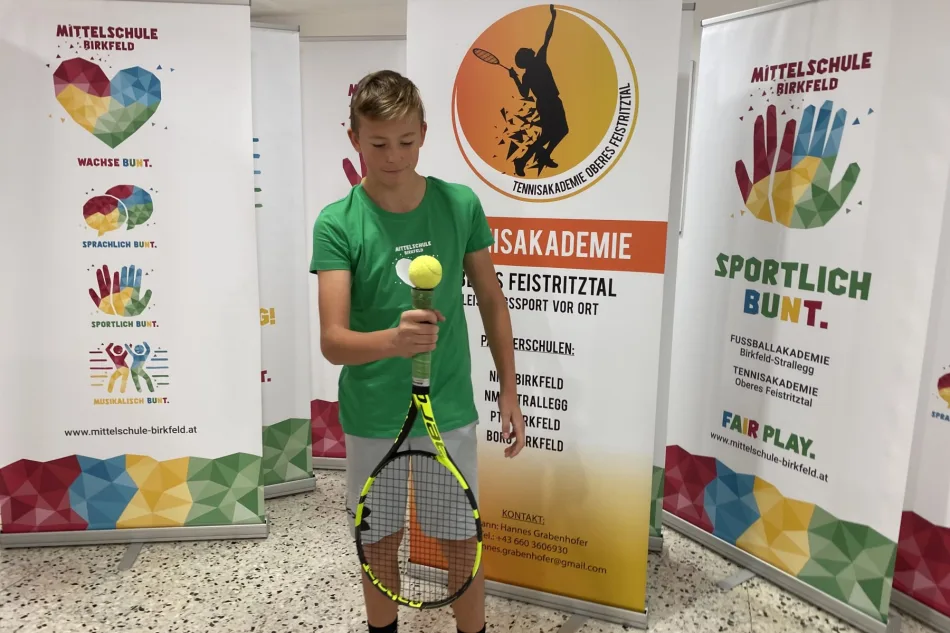 Foto: Mittelschule Birkfeld Schüler im grünen Shirt mit Tennisschläger und Ball vor dem Banner der Tennisakademie